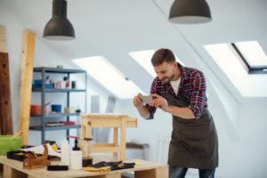 Male carpenter photographing with his smart phone chair he just made for client and sending to client by email or text message. Selective focus to smart phone. Shot with Canon EOS 5Ds with 50/1.2L 50 Mpx.