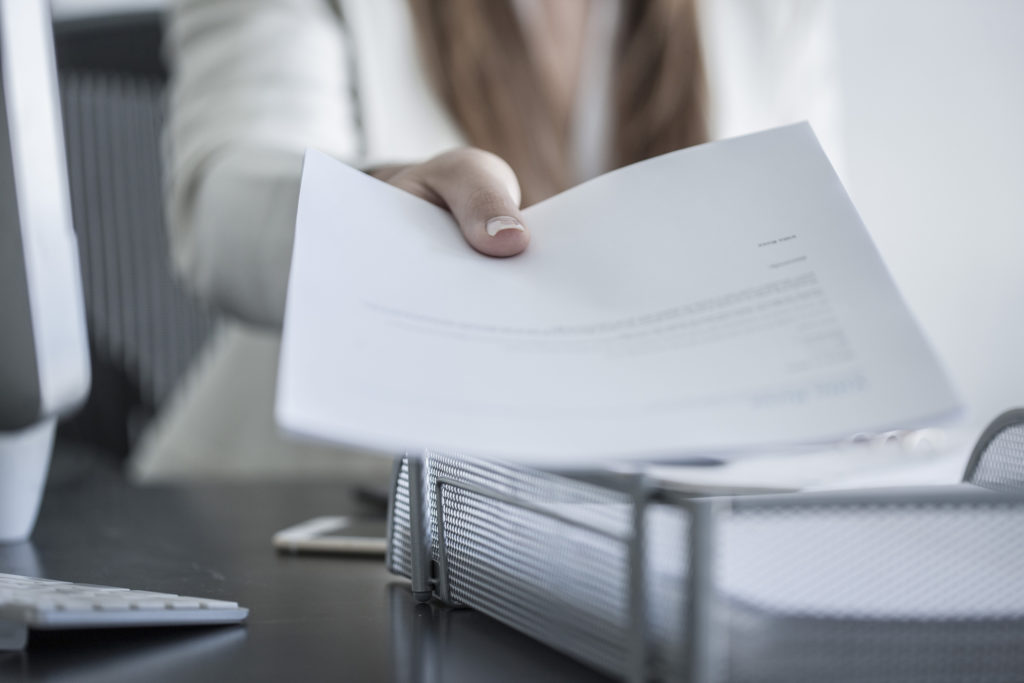 Close-up of woman at desk handing over a document