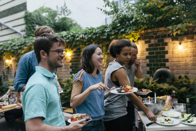 A group of friends having an evening barbecue together are loading their plates with food, hungry and ready to eat.