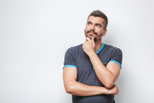 Portrait of handsome caucasian man with grey beard standing on white background. Man thoughtfully looking up