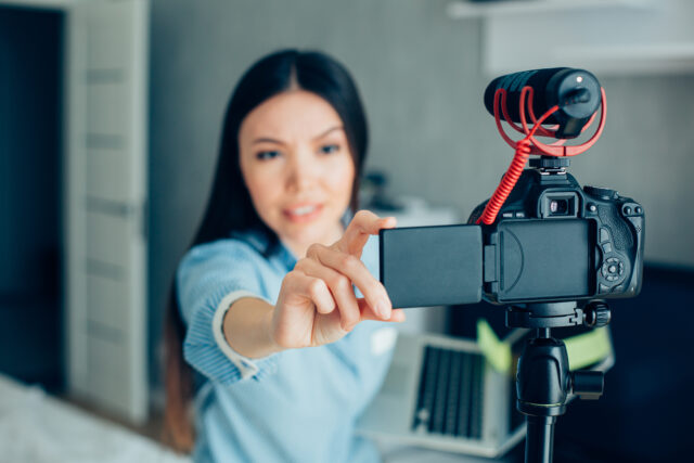Young Caucasian woman preparing for recording a video and touching a screen of a camera on tripod