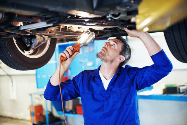 Automotive mechanic peering underneath a car while holding a lamp
