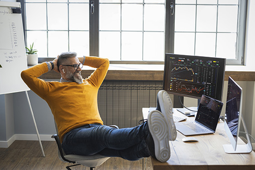 Mature businessman sitting at the table and working on computers. He is trading with cryptocurrency.