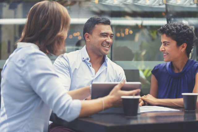 Happy couple having a business meeting with a financial advisor. They are looking at a laptop computer or digital tablet. They are an ethnic couple. They are happy and smiling.